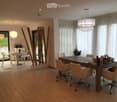 Open-plan dining and office area with modern furniture, large windows with curtains, and decorative wooden sculptures.