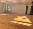 Empty room with wooden flooring, white walls, large windows, radiator, and a closed door.