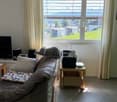 Living room with a sofa, a small table, a radio, a television, and a decorative pillow. The room features large windows with a scenic mountain view.