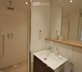 Modern bathroom with a glass-enclosed shower, a white sink with a wooden countertop, a large mirror, and a towel hanging on a rack.
