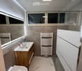 Modern bathroom with marble flooring, a wooden vanity with a sink, a toilet, a towel rack, and a large mirror with built-in lighting.