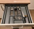 Open kitchen drawer with neatly organized cutlery including forks, knives, spoons, and scissors in separate compartments.