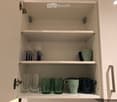 Open kitchen cabinet with multiple shelves displaying various cups and glasses neatly arranged.