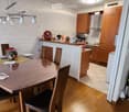 A modern kitchen and dining area with wooden cabinets, a round wooden dining table with chairs, and various kitchen appliances.