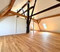 Empty attic space with wooden beams, wooden flooring, and skylight windows.