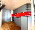 Modern kitchen with grey cabinets, red backsplash, wooden flooring, and built-in appliances including a sink, faucet, and oven.