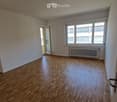 Empty room with wooden flooring, white walls, large windows, and a radiator under the windows.
