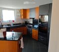 Modern kitchen with wooden and grey cabinets, black countertops, and stainless steel appliances. Features include a sink, oven, refrigerator, coffee maker, and a bottle on the counter.