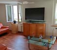 Modern living room with wooden flooring, a red leather sofa, a glass coffee table, a TV on a wooden stand, and a small plant on a side table.