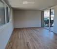 Empty room with wooden flooring and large windows, featuring a sliding glass door leading to an outdoor area.
