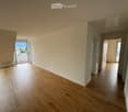 Empty room with wooden flooring, white walls, and large windows offering a scenic view. The room is unfurnished and has an open doorway leading to another room.