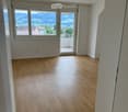 Empty room with wooden flooring, large windows, and a sliding glass door leading to a balcony.