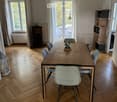 Dining room with wooden herringbone flooring, large windows with white curtains, a modern dining table with six chairs, a shelf unit, and a lantern on the floor.