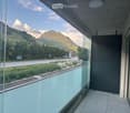 Modern balcony with glass railings, tiled floor, and scenic mountain view.