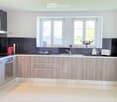 Modern kitchen with light wood cabinets, stainless steel appliances, and a sleek black backsplash. Features include a refrigerator, oven, sink, faucet, toaster, teapot, and decorative items on the counter and side table.