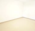 Empty room with white walls and light-colored flooring, featuring a partially open door and a visible door handle.