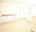 Empty room with white walls, light-colored tiled floor, and built-in white cabinetry with a wooden countertop. Three doors are visible.