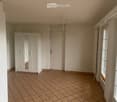 Empty room with tiled floor, white walls, large windows, and a white wardrobe with mirrored doors.