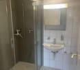 Modern bathroom with a glass-enclosed shower, white tiled walls and floor, a sink with a mirror, and a toilet.