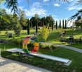 Outdoor area with lawn, scattered chairs and tables, a colorful play structure, and grazing horses in the background.
