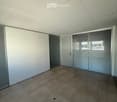 Empty room with tiled floor, white walls, large windows with blinds, and a door.