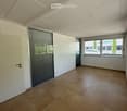Empty room with beige tiled floor, white walls, large windows with blinds, and a white door.