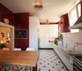 Modern kitchen with white cabinets, dark red walls, white tiled backsplash, and a wooden dining table with stools.