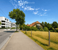 Residential street lined with modern apartment buildings and traditional houses, surrounded by greenery and trees.