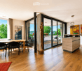 Bright, open-plan dining and kitchen area with wooden flooring, large windows offering a scenic view, a dining table with chairs, a kitchen island, and decorative art pieces.