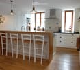 Bright, modern kitchen with white cabinets, wooden island, four bar stools, stainless steel appliances, and ample natural light from large windows.