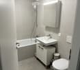 Modern bathroom with a bathtub, sink, mirror, and toilet. Features a white cabinet under the sink and a showerhead above the bathtub.
