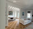 Open-concept living and dining area with a white sofa, dining table, chairs, and artwork on the walls.