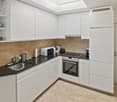 Modern kitchen with white cabinets, black countertop, stainless steel sink, microwave, oven, and refrigerator. Features a built-in hood and open shelving with decorative items.