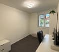 Modern office space with dark tiled floor, white walls, and a large window with blinds. Features a white desk with a screen, a black chair, and a white cabinet.