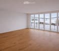 Empty room with wooden flooring and large sliding glass doors leading to a balcony with a view of a snowy landscape.