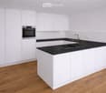 Modern kitchen with white cabinets, black countertops, and a wooden floor. Features an oven, sink, and faucet.