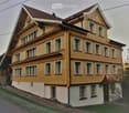 Two-story yellow house with multiple windows, red-tiled roof, and white trim around windows and roofline.