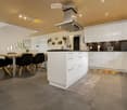 Modern kitchen with white cabinets, gray tiled floor, and a central island. Dining table and chairs are placed nearby.