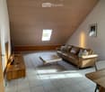Modern living room with a slanted wooden ceiling, large window, and skylight. Features a brown leather sofa, wooden coffee table, and a TV on a wooden stand.