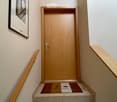 Wooden door with a silver handle, flanked by wooden handrails on both sides, with a small mat featuring a logo in front of the door.