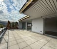 Modern balcony with tiled flooring, glass sliding doors, and potted plants, offering a scenic view of the surrounding landscape.