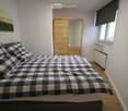 Cozy bedroom with a wooden floor, a large bed with a checkered duvet and pillows, a wooden wardrobe with a mirror, and a painting on the wall.