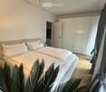 Modern bedroom with a large double bed, white pillows, a wardrobe, and a chandelier.