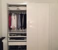 A modern, minimalist walk-in closet with white sliding doors, neatly organized clothes, and multiple storage compartments including drawers and shelves.