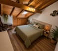 Cozy attic bedroom with wooden beams, skylight, bed with green bedding, nightstand, chair, and potted plants.