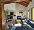 Cozy living room with exposed wooden beams, fireplace, large windows, sofa, coffee table, and television.