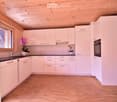 Modern kitchen with white cabinets, wooden ceiling, and wooden floor. Features a sink, faucet, oven, and two flower pots on the counter.