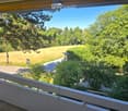 Balcony overlooking a lush, green landscape with trees, a road, and a grassy field.
