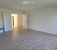Empty room with wooden flooring, white walls, and a fireplace on the left side. There are two open doors leading to other rooms.