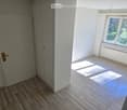 Empty room with wooden flooring, white walls, and a large window with a view of greenery. No furniture or equipment present.